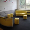 Lavice čalouněné žlutou koženkou doplněné válcovými taburetky slouží k relaxaci studentů během přestávek.